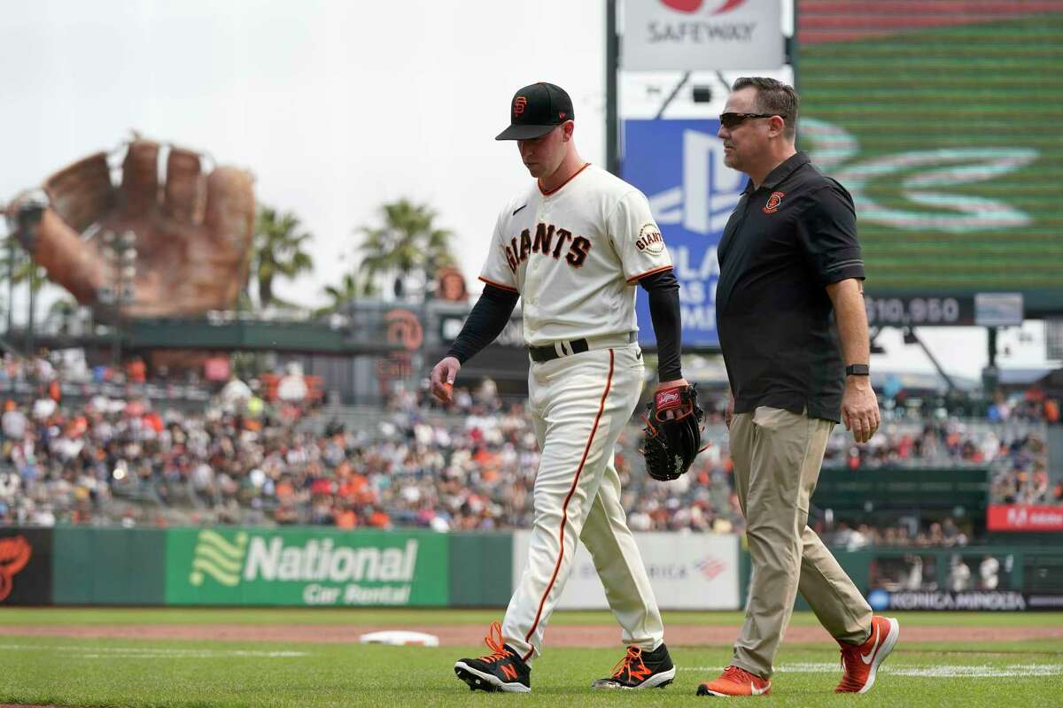 San Francisco Giants starting pitcher Anthony DeSclafani, left, walks off the field with trainer Dave Groeschner during the second inning of a baseball game between the Giants and the New York Mets in San Francisco, Wednesday, Aug. 18, 2021. (AP Photo/Jeff Chiu)