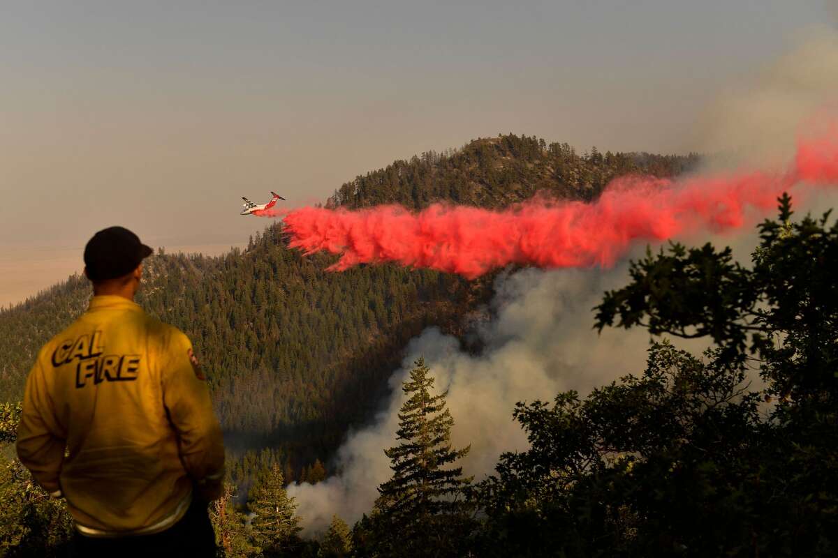A Cal Fire firefighter from the Lassen-Modoc Unit watches as an air tanker makes a fire retardant drop on the Dixie Fire as trees burn on a hillside on Aug. 18, 2021 near Janesville.