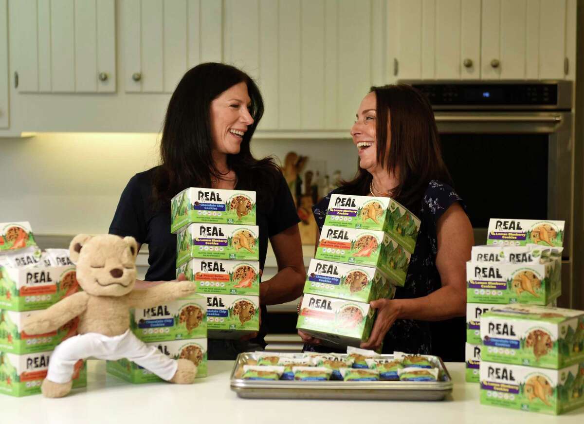 Get Real Foods co-owners Lauren Berger, left, and Maria Felton pose with their REAL cookies at Berger's home in Greenwich, Conn. Thursday, Aug. 12, 2021. REAL Cookies are a gluten-free, grain-free, plant-based cookie that come in three flavors - chocolate chip, peanut butter chocolate chip, and lemon blueberry.