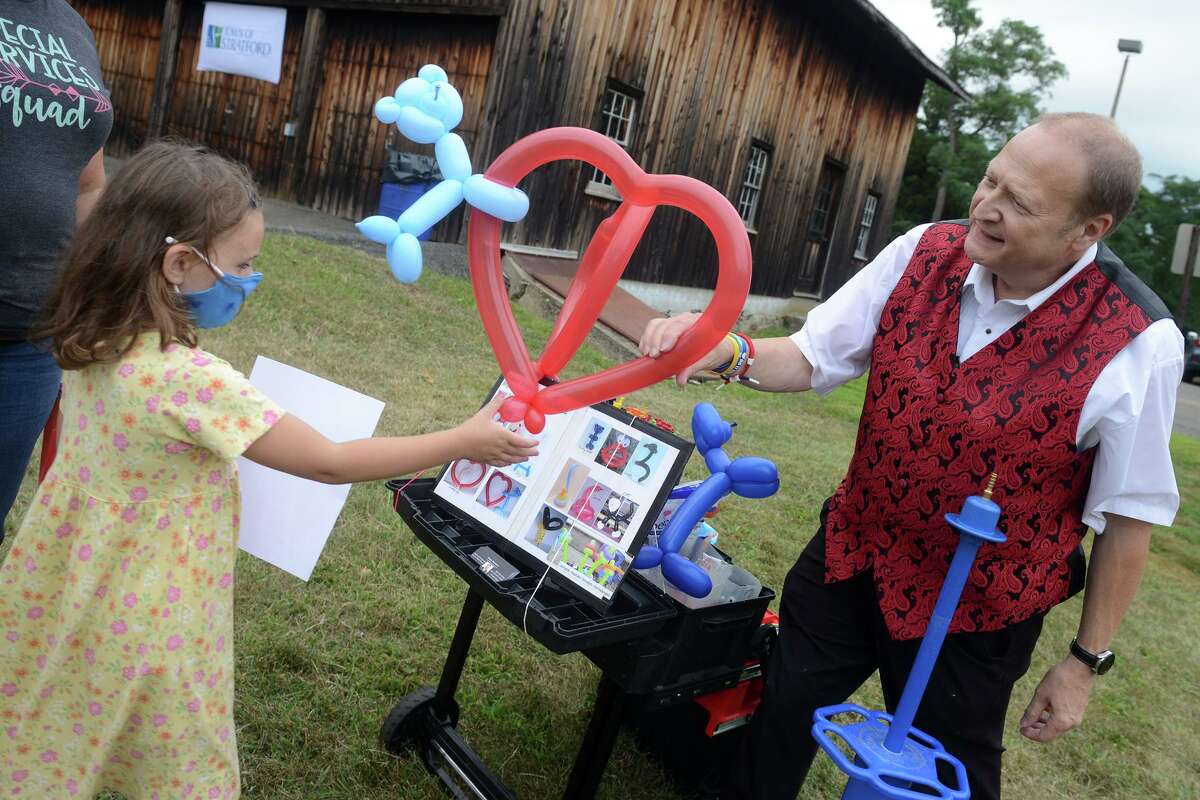 Chelsea Brelsford, age 6, receives a balloon from magician Bryant Lizotte during a season ending event for Mayor Laura Hoydick’s Summer Reading Challenge, in Stratford, Conn. Aug. 18, 2021.
