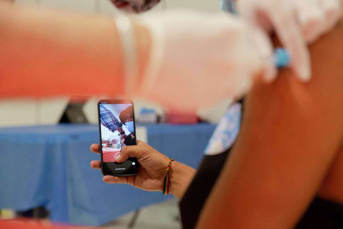 Franch Agustin takes a video for his mother while he receives the Johnson and Johnson COVID-19 vaccine at a vaccination site at the Solano Town Center mall in Fairfield, Calif.