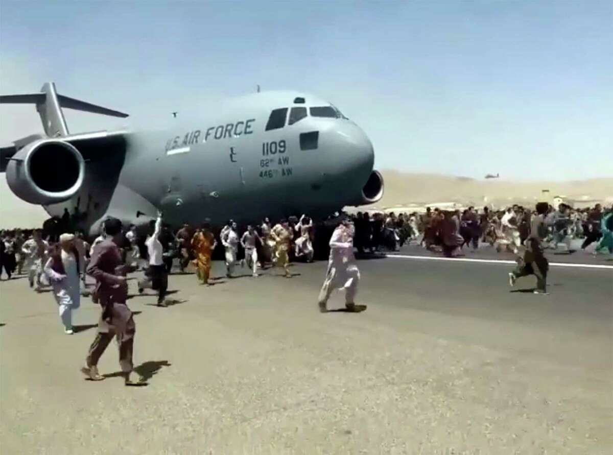 Hundreds of people run alongside a U.S. Air Force C-17 transport plane as it moves down a runway of the international airport, in Kabul, Afghanistan. They are helping to flee the Taliban.
