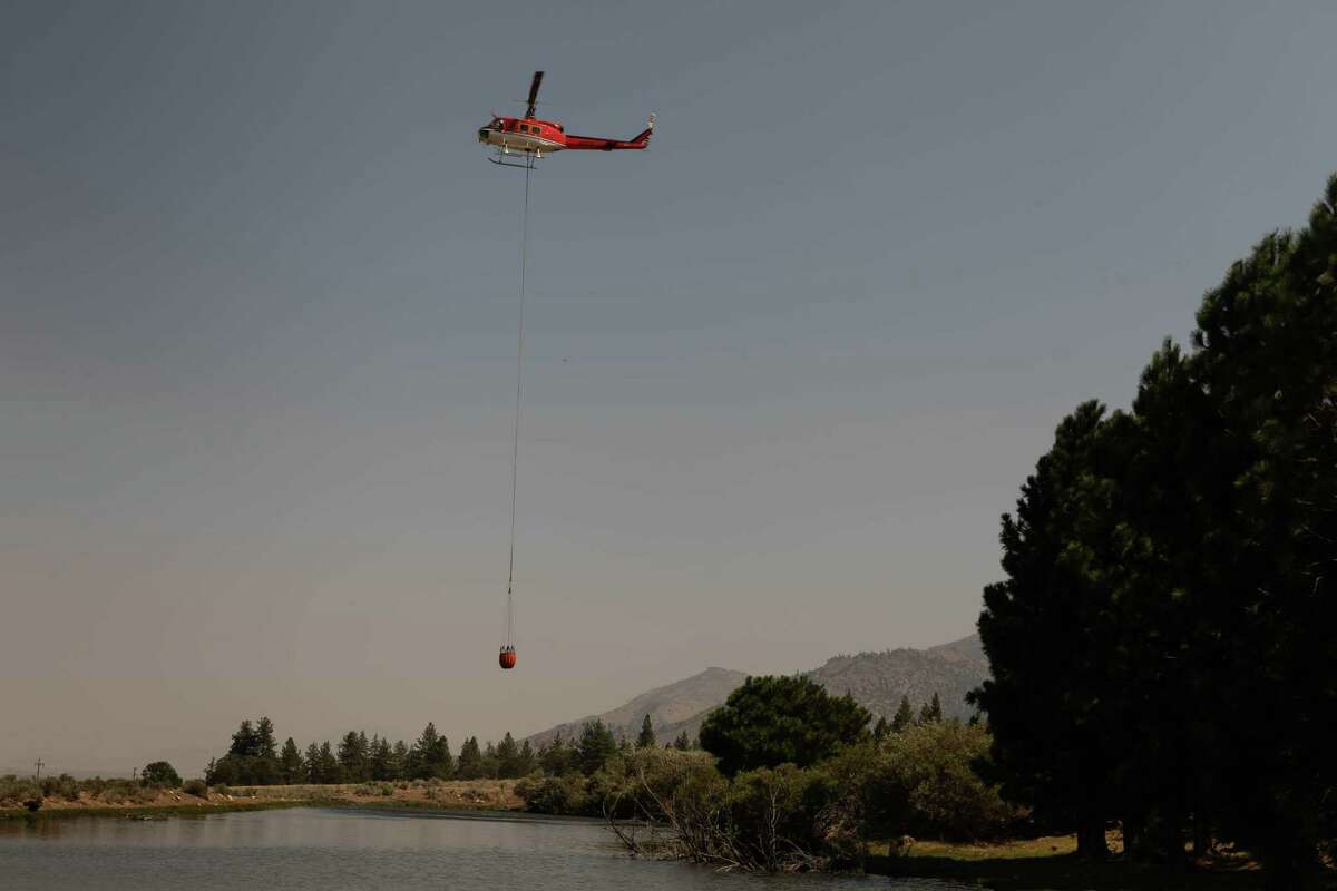 A helicopter gathers water from a farmer’s pond and carries it toward the Dixie Fire burning north of Milford on Wednesday.