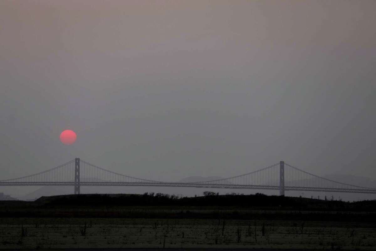 An orange sun sets in a hazy sky behind the Bay Bridge on Aug. 18, seen from Alameda. The Bay Area Air Quality Management District issued Spare the Air alerts as smoke from Northern California wildfires drifted into the region.