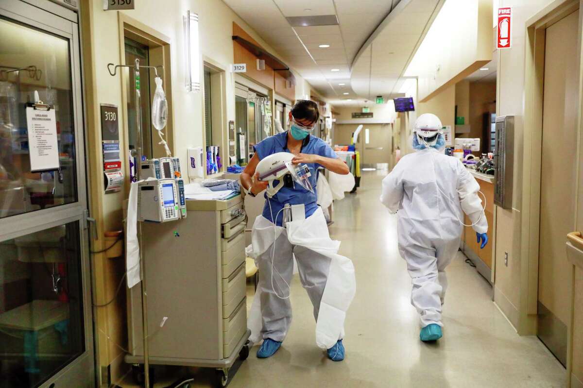 Nurse Shannon Baker (left) dons PPE before seeing a COVID-19 patient at El Camino in Mountain View.