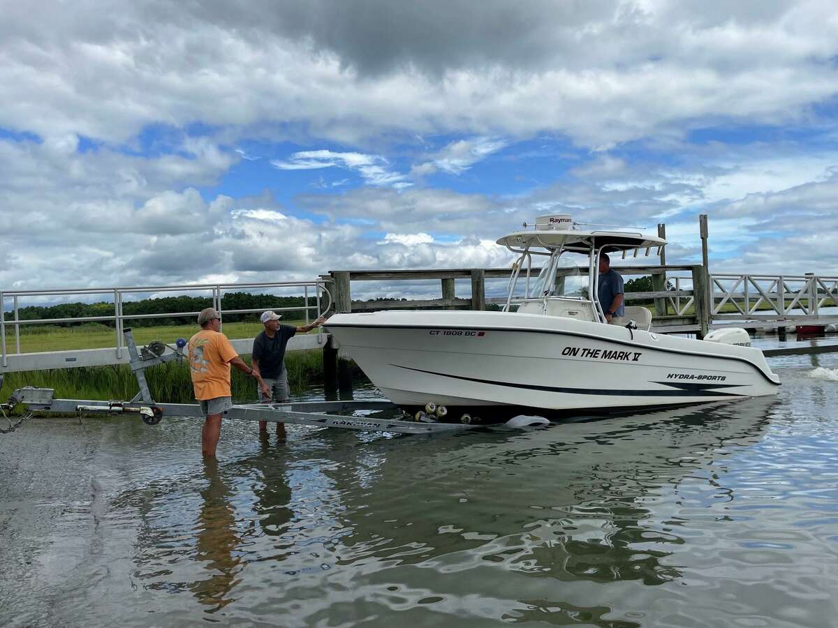 As Tom Markiewicz steers the boat, (l-r) Cliff Johnson and James Catlin guide him onto the trailer at the Guilford Boat Launch to get his boat out beforethe storm.