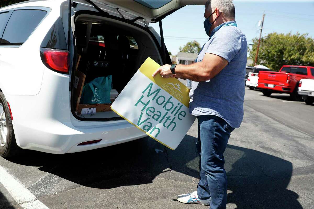 Contra Costra Health Services’ Ernesto De La Torre puts a magnetic sign on side of mobile health van after arriving at Cielo Market to give COVID vaccinations in Antioch, Calif.