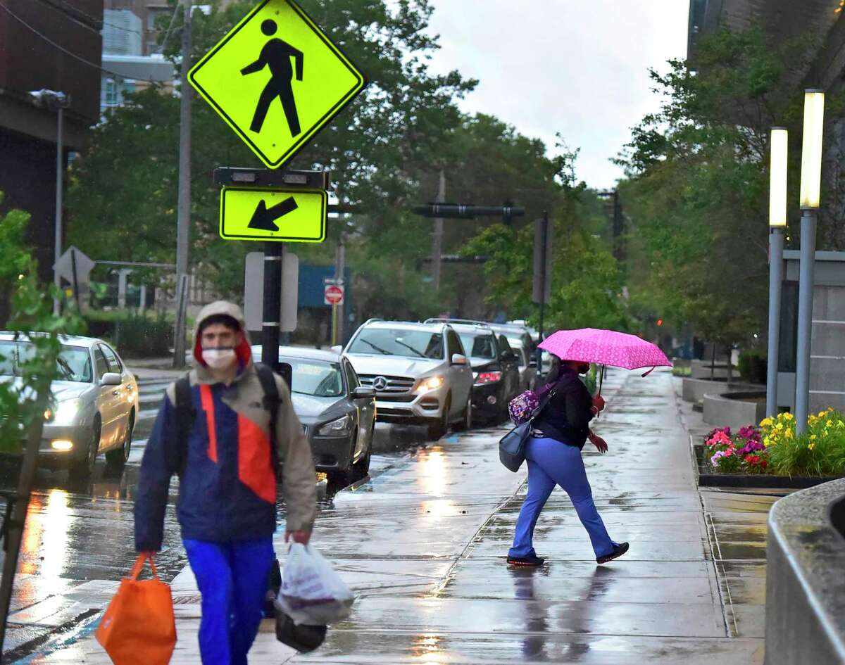 New Haven, Connecticut - Sunday, August 22, 2021: Pedestrians navigate the sidewalk in front of the Smilow Cancer Center in New Haven early Sunday morning as Hurricane Henri dropped only rain in the greater New Haven area.