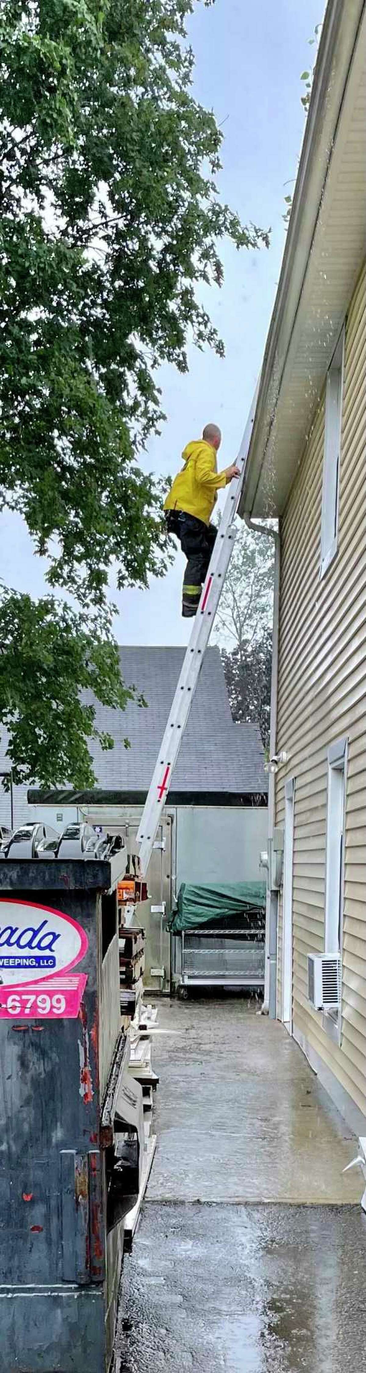 A member of the Torrington Fire Department climbs a ladder to clear a clogged gutter at Friendly Hands Food Bank Monday. Staff members discovered that the clogged gutter had caused flooding inside the building on King Street.