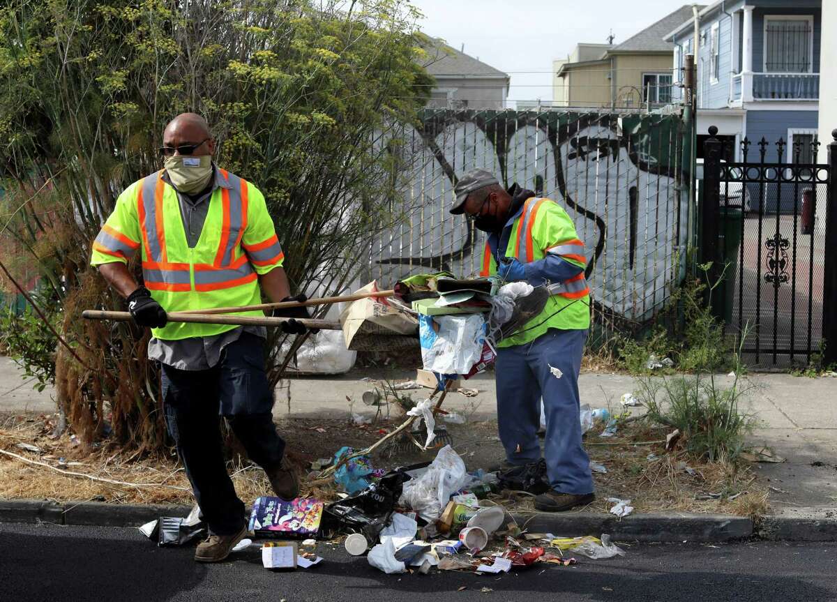 Marcus Leggett (left), a street maintenance leader, and Ayinde Osayaba, a street maintenance worker, pick up trash in Oakland. They are part of a team that drives through areas of Oakland that are known hot spots for illegal dumping.