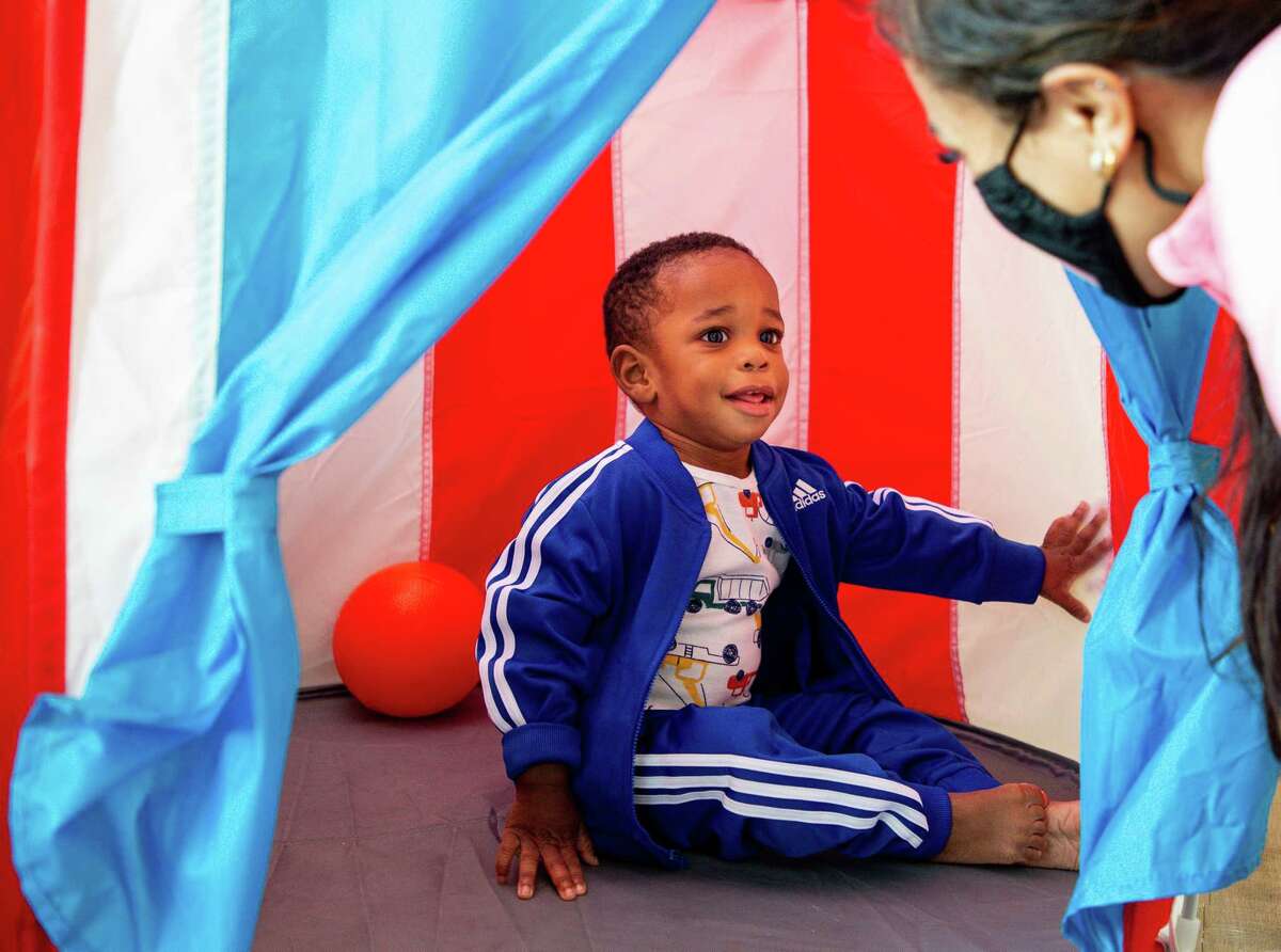 Emmanuel Odunuga, center, placed his hand on a tent wall to spot Cecilia Martinez's - a speech language pathologist assistant - hand while working on speech therapy at Joycare Pediatric Day Health Center on Friday, Aug. 13, 2021, in Houston. Odunuga was born with congenital syphilis and is now in physical and speech therapy four times a week.