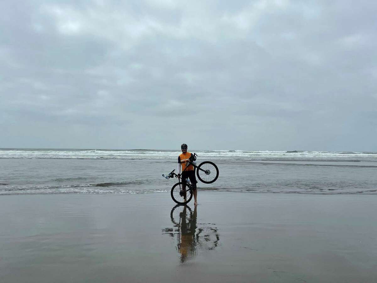 Alan Masarek dips his rear wheel in the Pacific Ocean to begin his 3,800-mile cross-country bike ride to raise awareness and funds for Empower House.