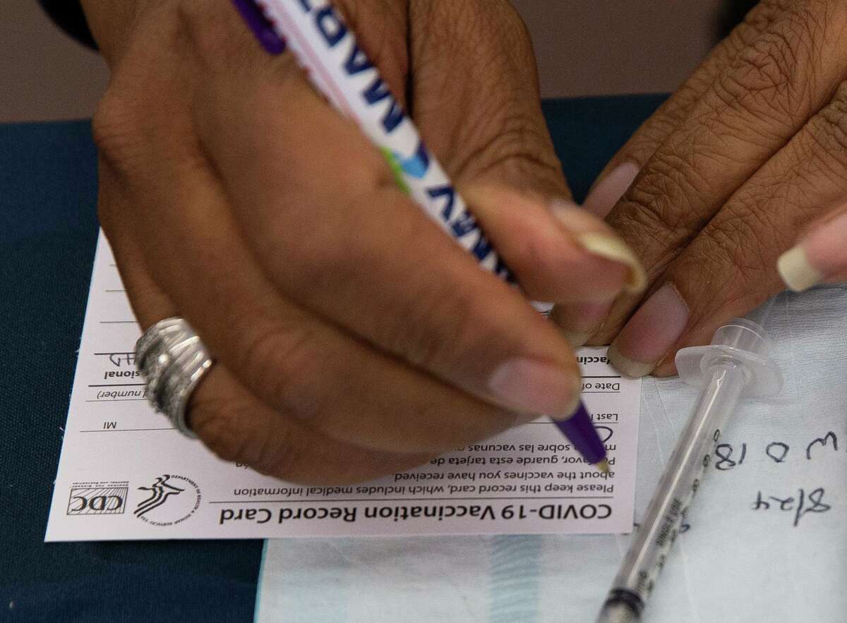 Ihsan Baha, a LVN at Houston Health Department, filling out a vaccine card for a woman who is receiving her first dose of COVID-19 vaccine at a Food Town market Tuesday, Aug. 24, 2021, in Houston.