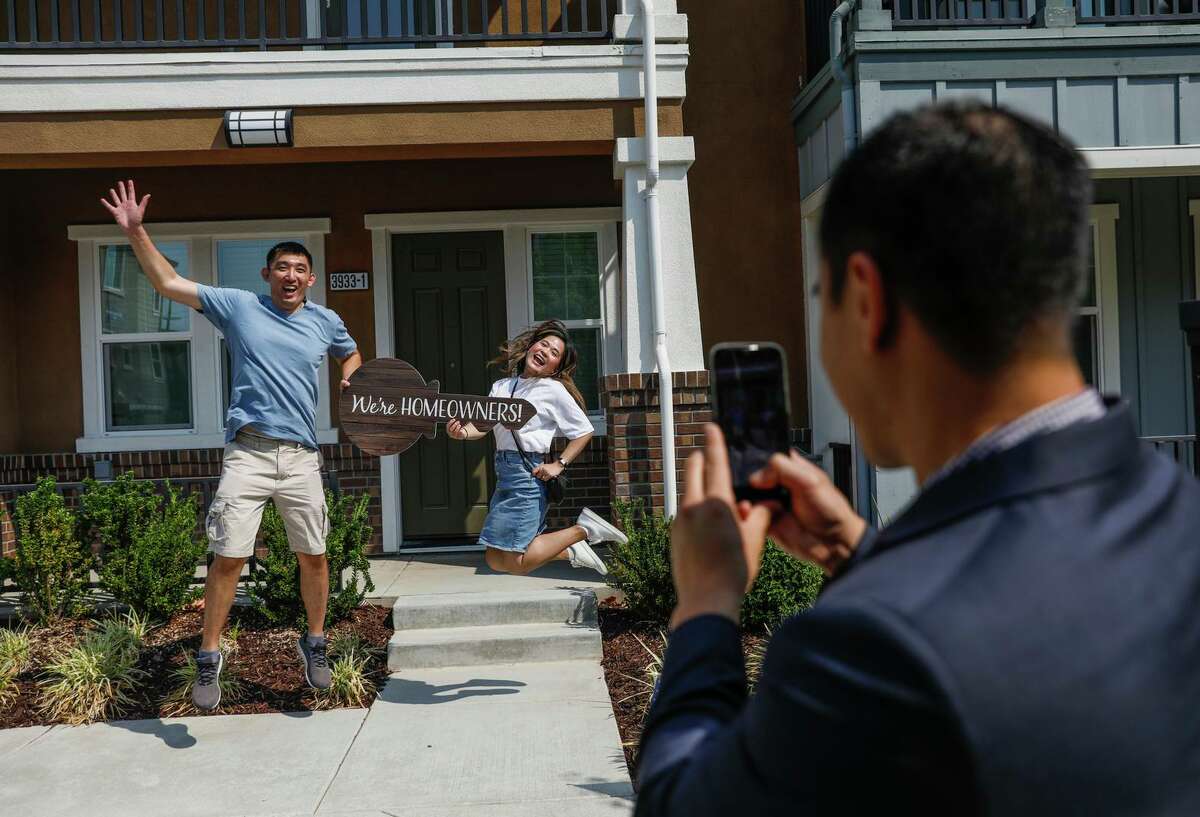 Realtor Scott Nguyen (right) photographs new homeowners Martin Wong (left) and Jann Ton at their newly purchased home. Nguyen carries a “We’re Homeowners!” sign to every home inspection and takes a photograph for clients to upload to social media.