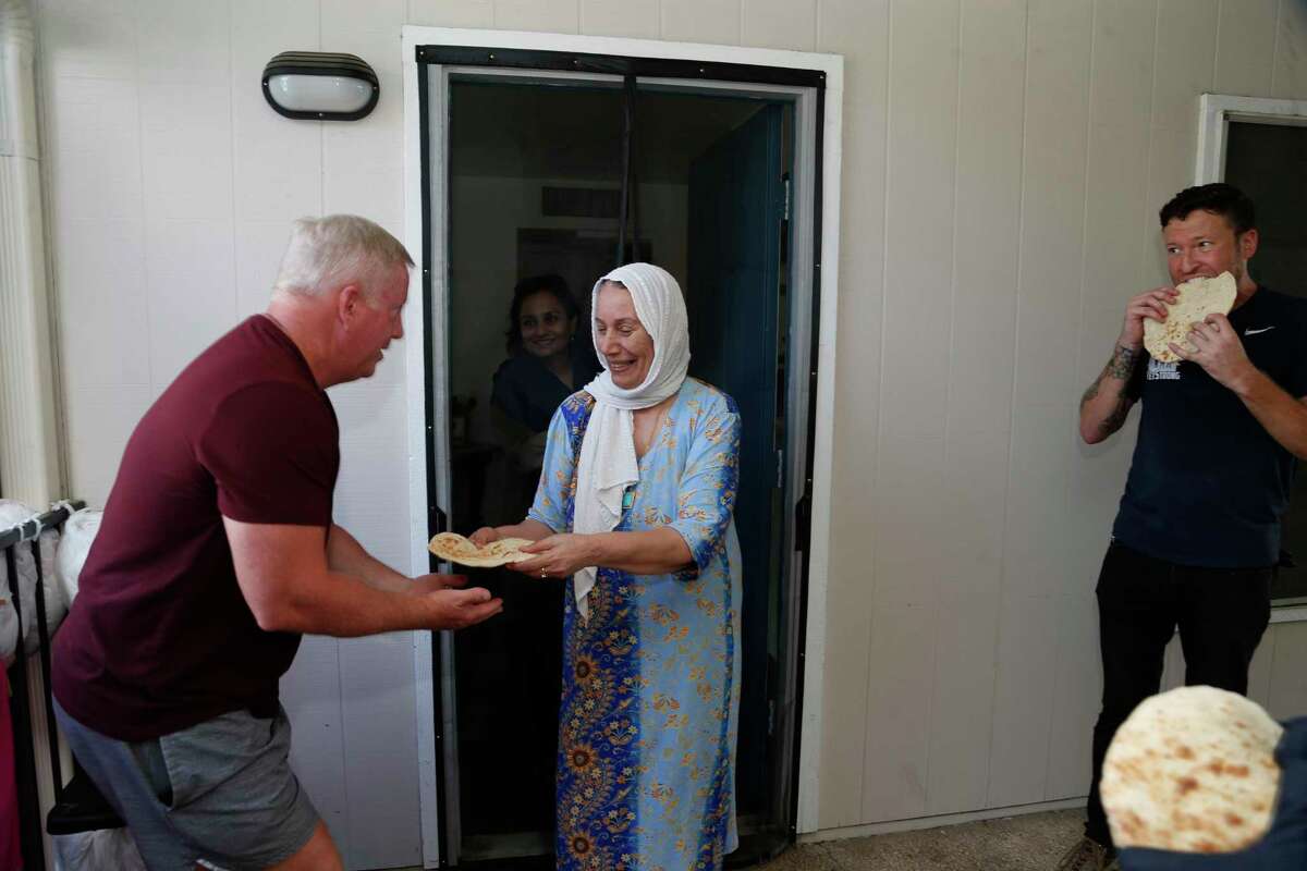 Iraq refugee Buzdan Farhan thanks veterans who moved a bed into her apartment by offering them bread at the Wurzbach Manor apartments on Saturday, Aug. 28,2021. On the left is volunteer Minder Huff. ASt right is veteran Erwin Frantti.