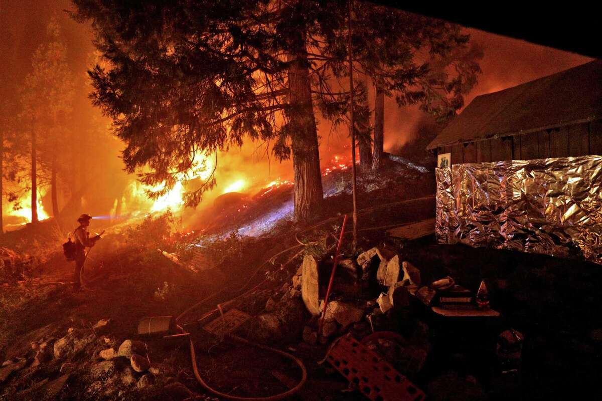 A firefighter monitors a back burn along Highway 50 next to a home that was partially wrapped in foil as crews continued structure prevention at the Caldor Fire in Strawberry, Calif.