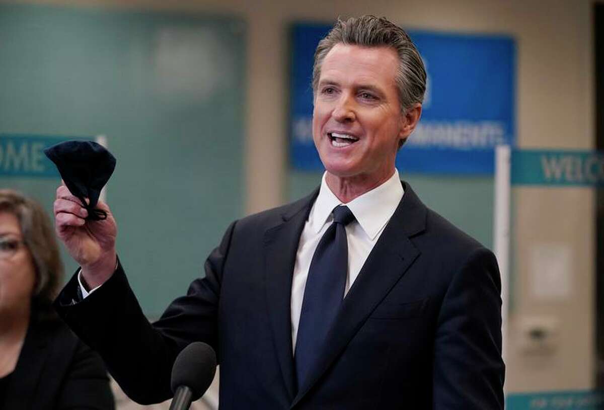 Gov. Gavin Newsom holds a face mask while speaking at a news conference in July in Oakland. Organizations that successfully sued the governor over pandemic-era limits on free assembly are being reimbursed for their legal expenses.