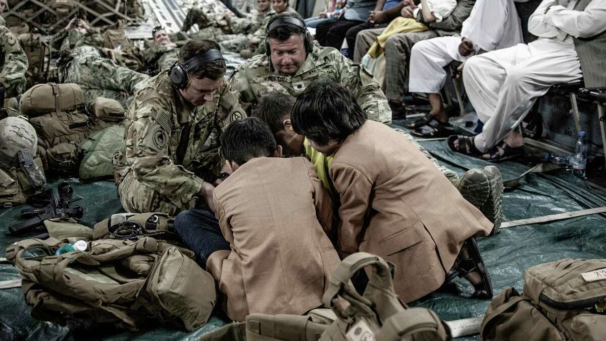 In this image provided by the U.S. Marine Corps, a soldier with Joint Task Force-Crisis Response plays a game on a phone with the children onboard a Boeing C-17 Globemaster III during an evacuation at Hamid Karzai International Airport in Kabul, Afghanistan, on Monday.