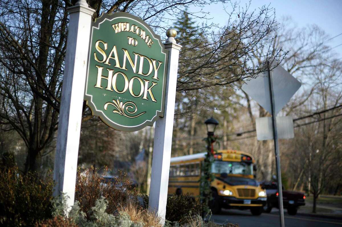 In this Dec. 4, 2013 file photo, a school bus drives past a sign reading Welcome to Sandy Hook, in Newtown, Conn., where 26 people were killed by a gunman inside Sandy Hook Elementary School. 