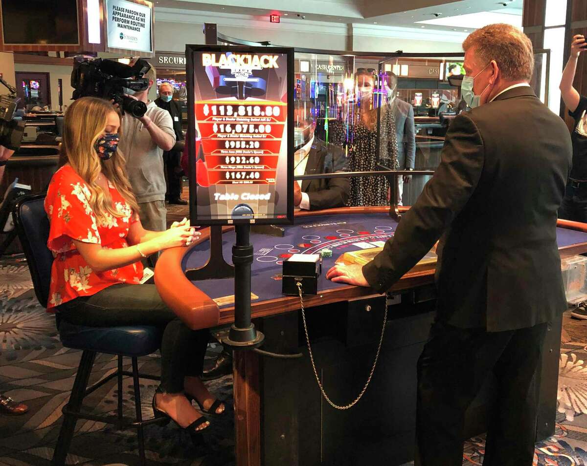 In this May 22, 2020 photo, a blackjack dealer at Foxwoods Resort Casino in Mashantucket, Conn., demonstrates to reporters on how new protective measures, including plastic shields, will work when the tribal-owned Foxwoods and neighboring Mohegan Sun expect to partially reopen on June 1. The Mashantucket Pequot and Mohegan Tribes are pushing ahead with plans to open their resorts on tribal lands, despite opposition from Connecticut Gov. Ned Lamont. (AP Photo/Susan Haigh)