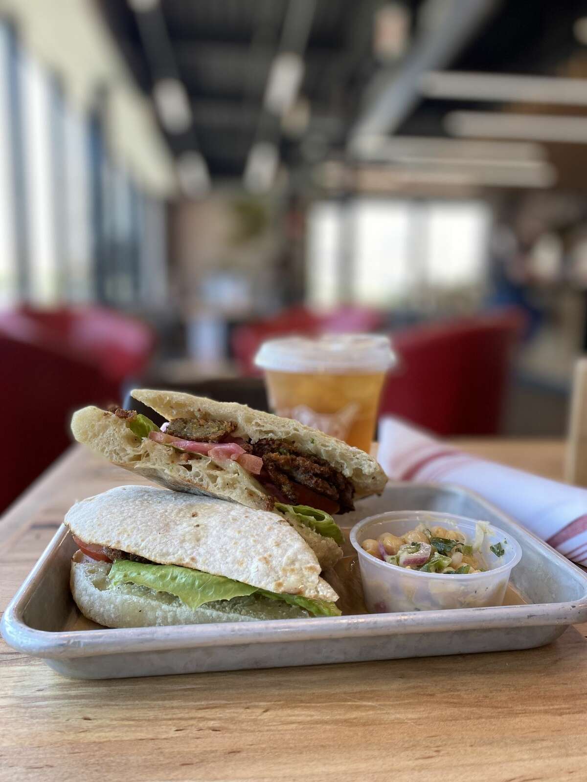 A falafel sandwich on housemade panini bread, highlighted by lettuce, tomato, pickled onions and lime tahini sauce.