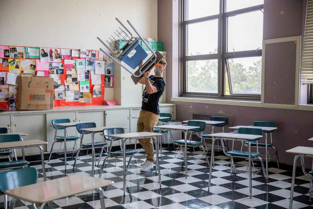 Braden DeWitt begins to arrange desks for physical distancing inside his classroom at McClymonds High School, Friday, Aug. 6, 2021, in Oakland, Calif. DeWitt has taught Spanish to juniors and seniors at the school for the last three years. He prepares to teach in-person at the school on Monday.