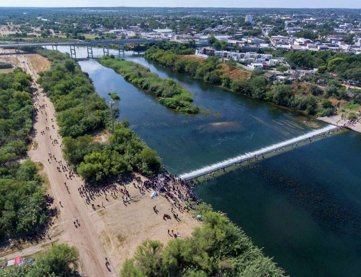 Migrants pass back-and-forth on a weir dam on the Rio Grande Thursday from Ciudad Acuña, Mexico, into Del Rio, Texas, right, as they wait to be processed by immigration officials under the nearby international bridge between the two cities. Thousands of migrants are waiting at the bridge to be processed by the Border Patrol
