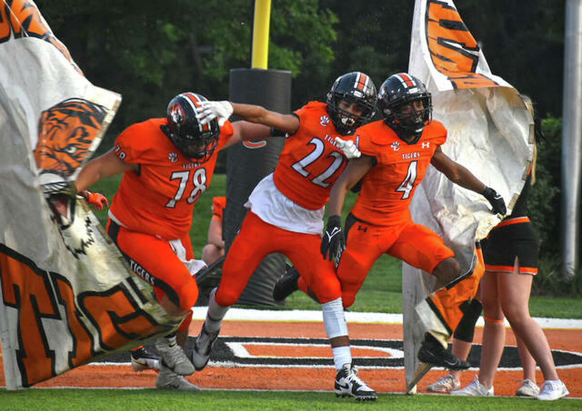 Edwardsville’s Dawson Rull, left, Kareem Haroun, center, and Kellen Brnfre break through the banner to lead the team onto the field for the Week 3 home opener against Champaign Central on Friday inside the District 7 Sports Complex.