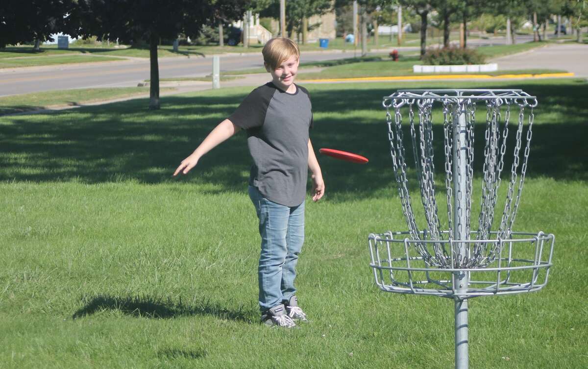 An Armory Youth Project student tosses a disc at the basket during the first day of the Armory's disc golf program in Manistee on Wednesday.