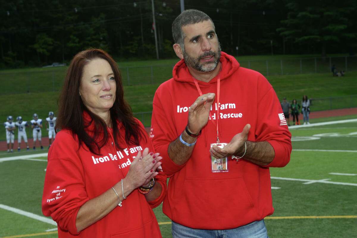 Ryan Rutledge’s parents, Valeria and Anthony, applaud while members of the Pomperaug High School football team are introduced prior to a game in Southbury, Conn. Sept. 17, 2021. Rutledge, who was a member of the Pomperaug football team, was killed in an automobile accident in April.