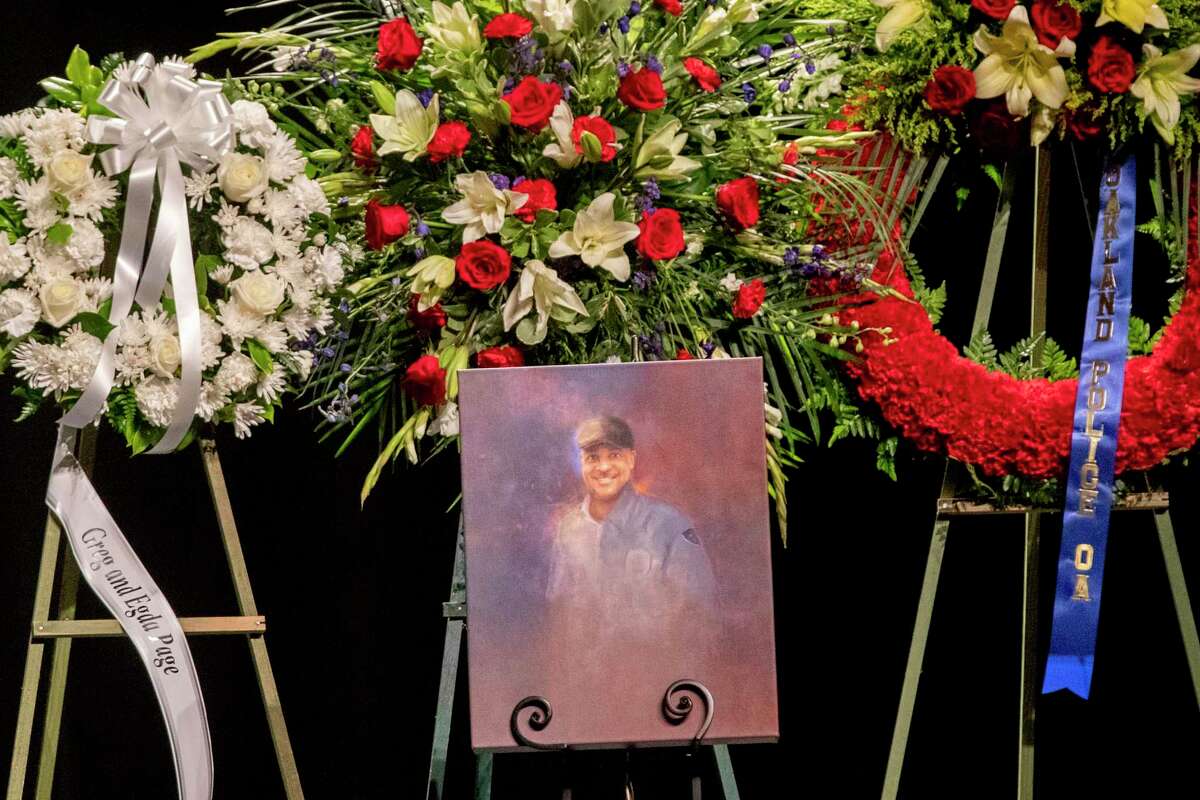 A painting sits near large displays of flower wreaths during a 2020 memorial service at Pinole High School for Dave Patrick Underwood, a contract security officer for the Department of Homeland Security who was shot and killed while guarding the Ronald V. Dellums Federal Building in Oakland.