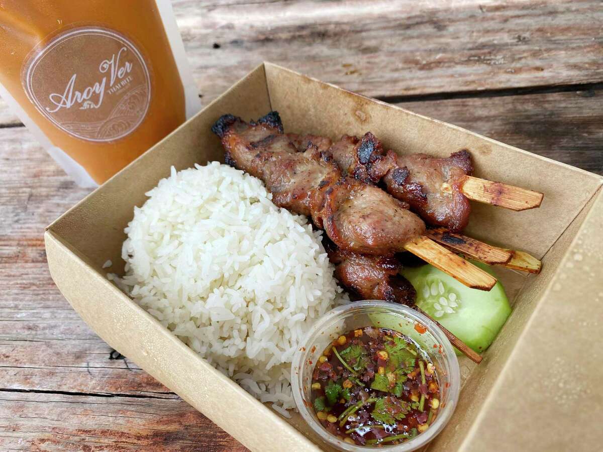 Grilled pork skewers called moo ping come with rice and Thai chile sauce, and Thai tea is served in a sealed bag like a juice pouch at Aroy Ver, a Thai food trailer parked on Broadway north of the Pearl at Broadway News.