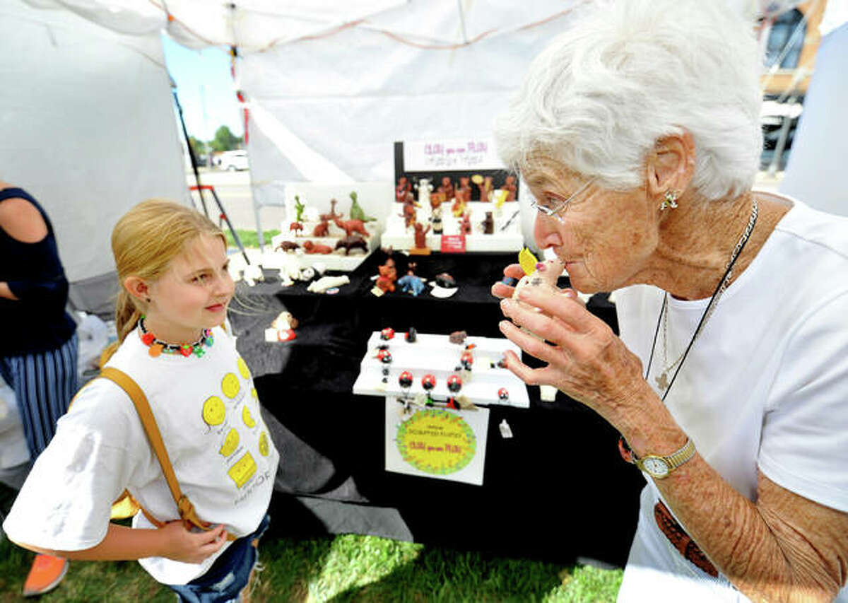 Madi Cameron, 10, of Maryville (left) listens to Doris Trojcak of St Louis play one of her clay animal flutes at Trojcak’s tent during the Edwardsville Art Fair in City Park Saturday.