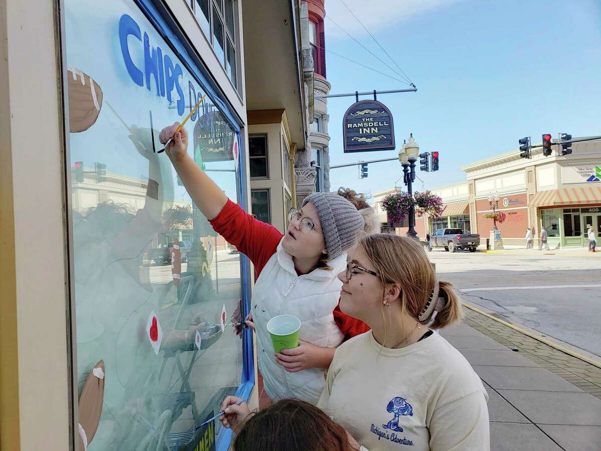 Kaylee Loper (front) and Flynn Anderson work on the Manistee High School freshmen class homecoming window art on Saturday on River Street. (Arielle Breen/News Advocate)