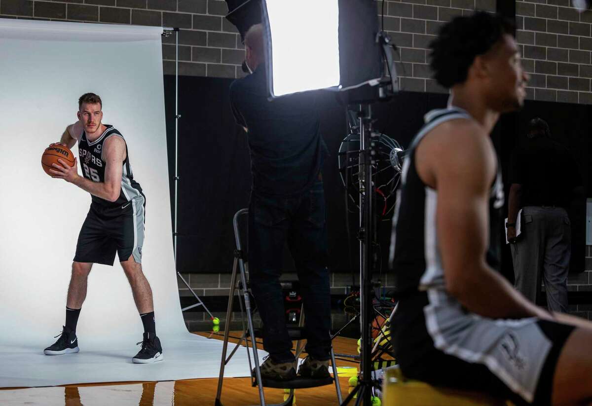 Spurs guard Jakob Poeltl, left, poses for photos Monday, Sept. 27, 2021 at the Spurs practice facility during the team's media day while teammate Keldon Johnson, right, does an interview.