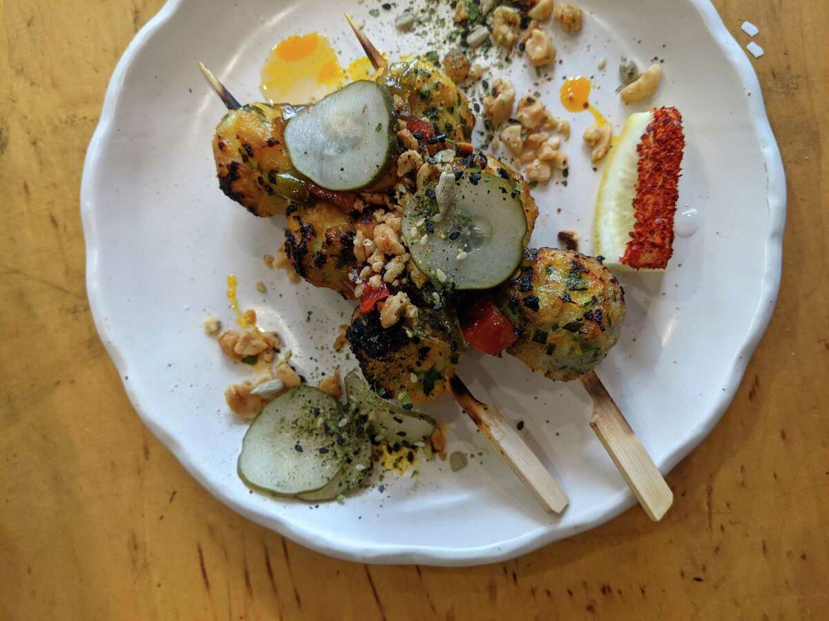 Grilled fish ball skewers, a Filipino street food staple, topped with annatto chili oil and garlic vinegar peanuts at Ox & Tiger in San Francisco.