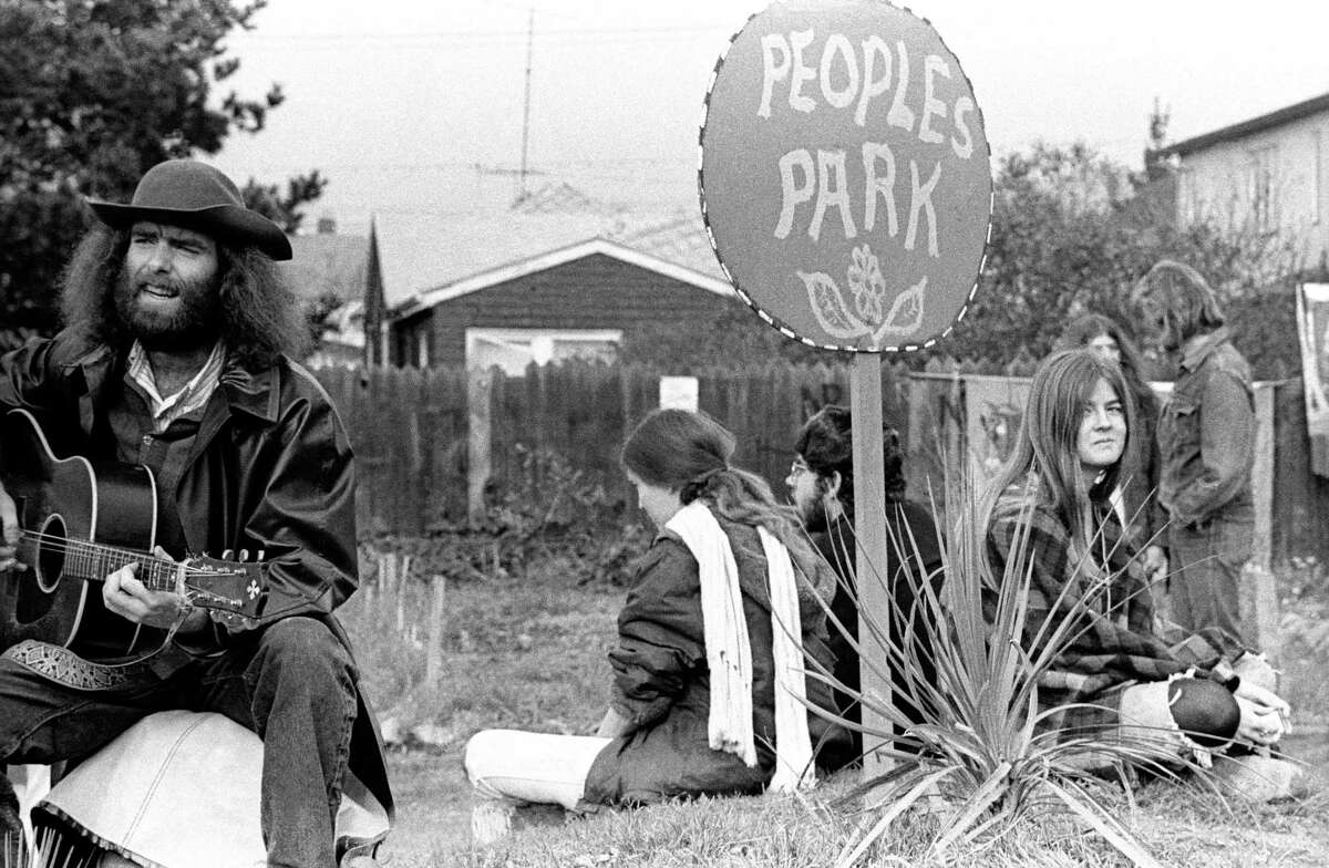 在这张大约1970年的照片中，一名男子弹着吉他，其他人围着一个写着“人民公园”的标志。