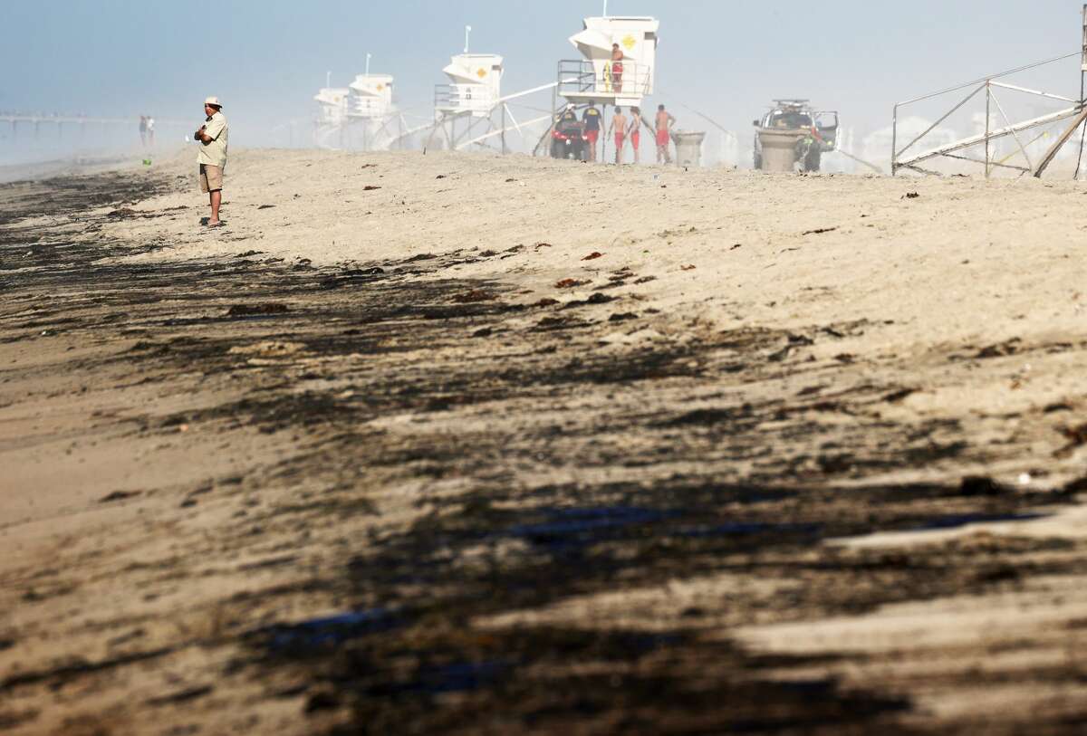 A person stands near oil washed up on Huntington State Beach after a 126,000-gallon oil spill from an offshore oil platform on Oct. 3, 2021, in Huntington Beach, Calif.