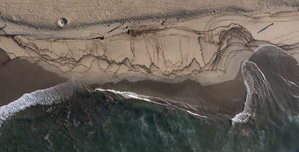 An aerial view of a major oil spill washing ashore with birds feeding at the water's edge on the border of Huntington Beach and Newport Beach at the Santa Ana River Jetties on Sunday, Oct. 3, 2021, in Huntington Beach, Calif.
