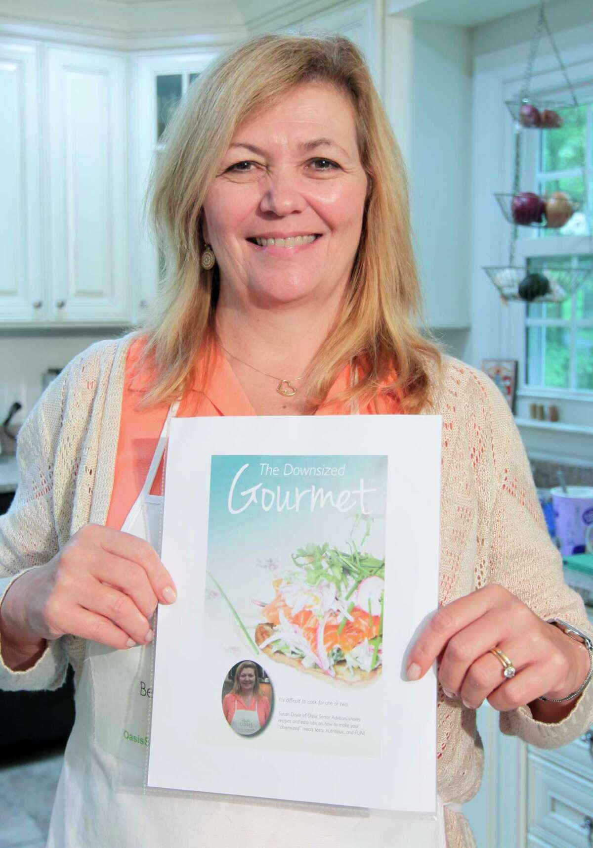 Susan Doyle, who uses Zoom to broadcast her show: Downsized Gourmet, poses with the cover of her upcoming cookbook in her kitchen at her home in Stamford, Conn., on Tuesday October 5, 2021. Due to the COVID-19 pandemic, in June of 2020 Susan and her husband Paul, who takes care of all things tech related, started the cooking show and invited members of several senior centers and facilities to tune in. Their work has culminated in the cookbook which will raise money for the Fairfield County Walk to End Alzheimer's slated for Sunday October 10th.