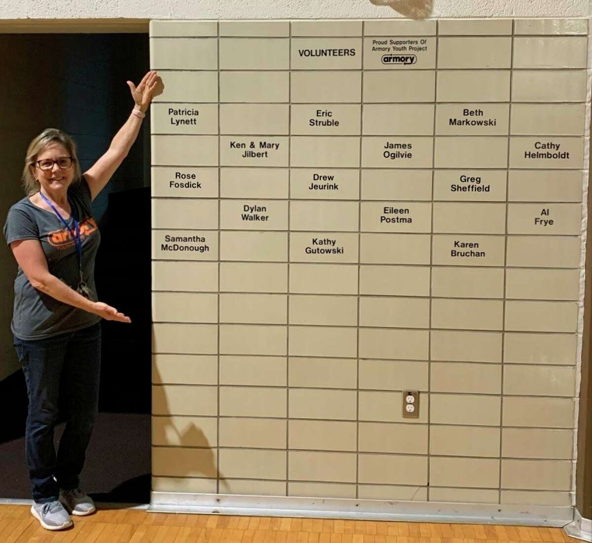 Amy Wojciechowski, Armory Youth Project executive director, shows off the Wall of Service which features the names of volunteers who have provided over 150 hours of service in the past year. (Courtesy photo)