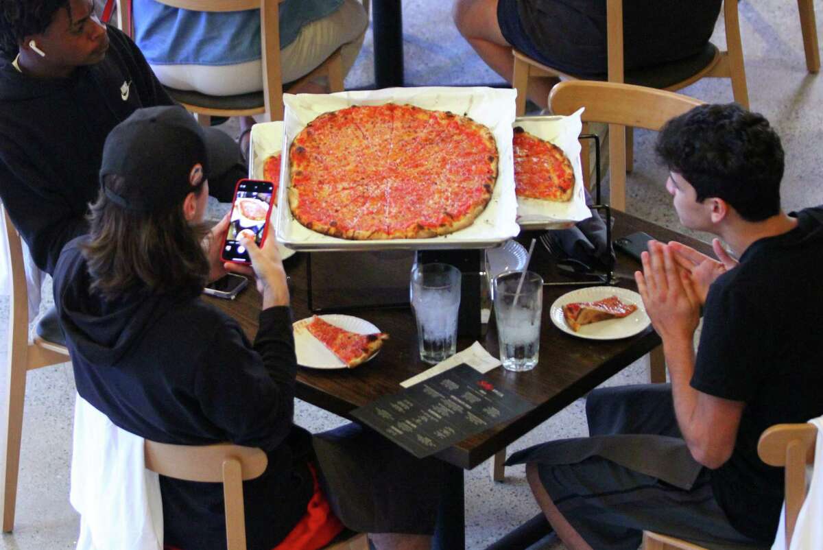 A customer snaps a picture of a pizza just brought to the table during the grand opening of Sally's Apizza on Summer Street in Stamford, Conn., on Thursday October 7, 2021. This is the new outpost of the beloved New Haven pizza restaurant.