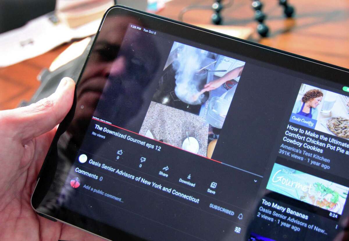 Paul Doyle, who helps his wife Susan use Zoom to broadcast her show: Downsized Gourmet, shows a past show posted to YouTube in the kitchen of their home in Stamford, Conn., on Tuesday October 5, 2021. Due to the COVID-19 pandemic, in June of 2020 Susan started the cooking show and invited members of several senior centers and facilities to tune in. Their work has culminated in a cookbook which will raise money for the Fairfield County Walk to End Alzheimer's slated for Sunday October 10th.