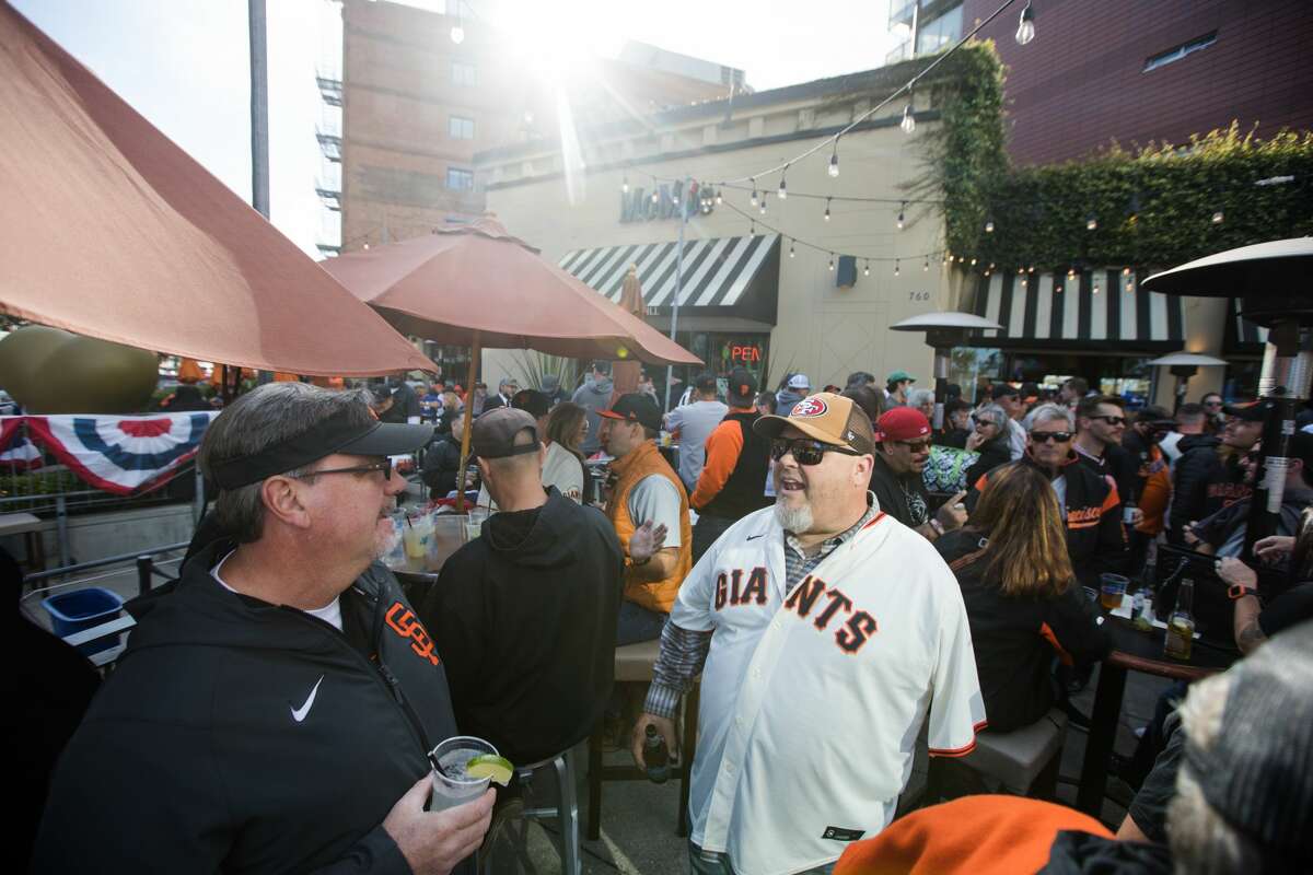 San Francisco Giants fans Vic Gets (left) and Jeff Markley (center) grab a drink on the packed outdoors patio at MoMo's, a sports bar and restaurant which sits across the street from Oracle Park in San Francisco, California, on Oct. 8, 2021 before game one of the National League Division Series.