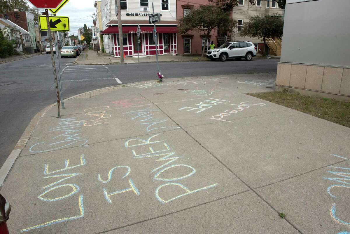 Messages are written in chalk on the sidewalk at the scene of Saturday night’s mass shooting that killed Alexander Bolton and wounded six people on Monday, Oct, 11, 2021 in Albany, N.Y. A bullet hole is seen on the building at right. The shooting happened at the Lounge located at 117 North Lake Ave.
