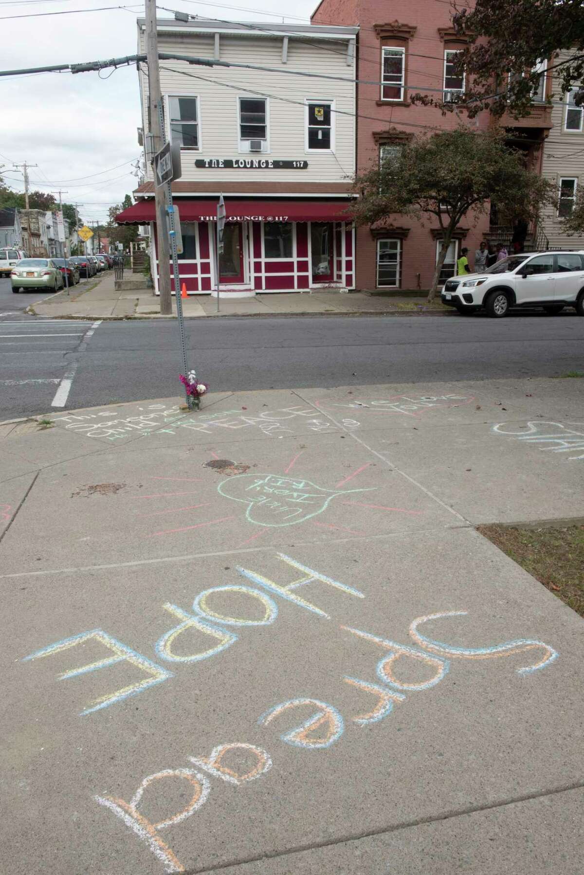 Messages are written in chalk on the sidewalk at the scene of Saturday night’s mass shooting that killed Alexander Bolton and wounded six people on Monday, Oct, 11, 2021 in Albany, N.Y. A bullet hole is seen on the building at right. The shooting happened at the Lounge located at 117 North Lake Ave.