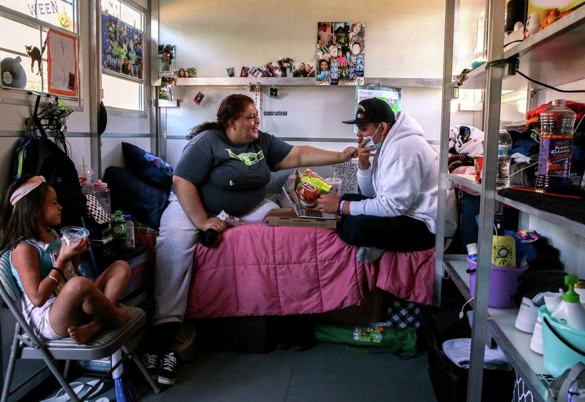 Maria Castañeda, left, sits in her tiny home with her 15-year-old son Angel Odilon, right, and neighbor Ximena Diaz, 6, while at Casitas de Esperanza shelter in San Jose, Calif., on Sunday, Oct. 10, 2021. Currently, there are about 538 homeless families in Santa Clara County, where officials hope that one-time pandemic funding and rethinking of housing vouchers will help house homeless families by 2025.