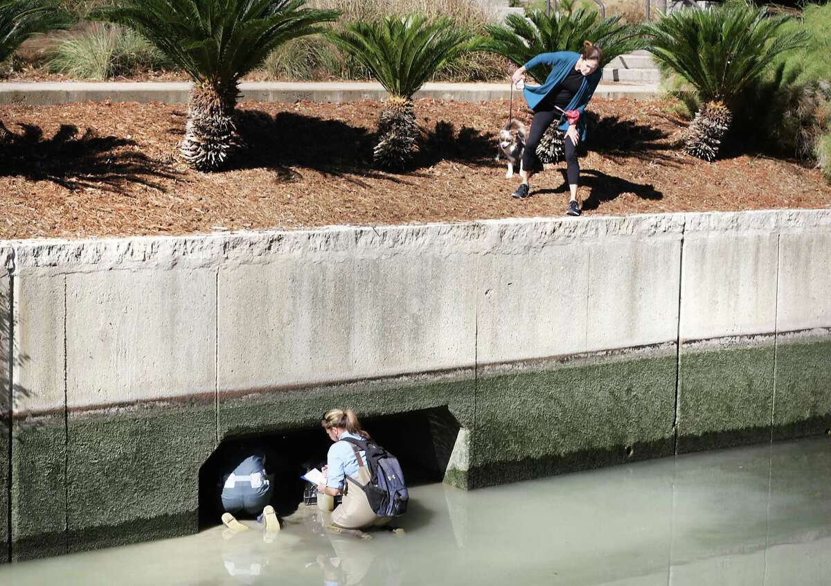 A woman walking her dog along the San Antonio River last year peers over the edge to look at San Antonio River Authority Biologist Karen Sablan, right, and Alicia Ramsey taking water samples as the river is drained for cleaning.