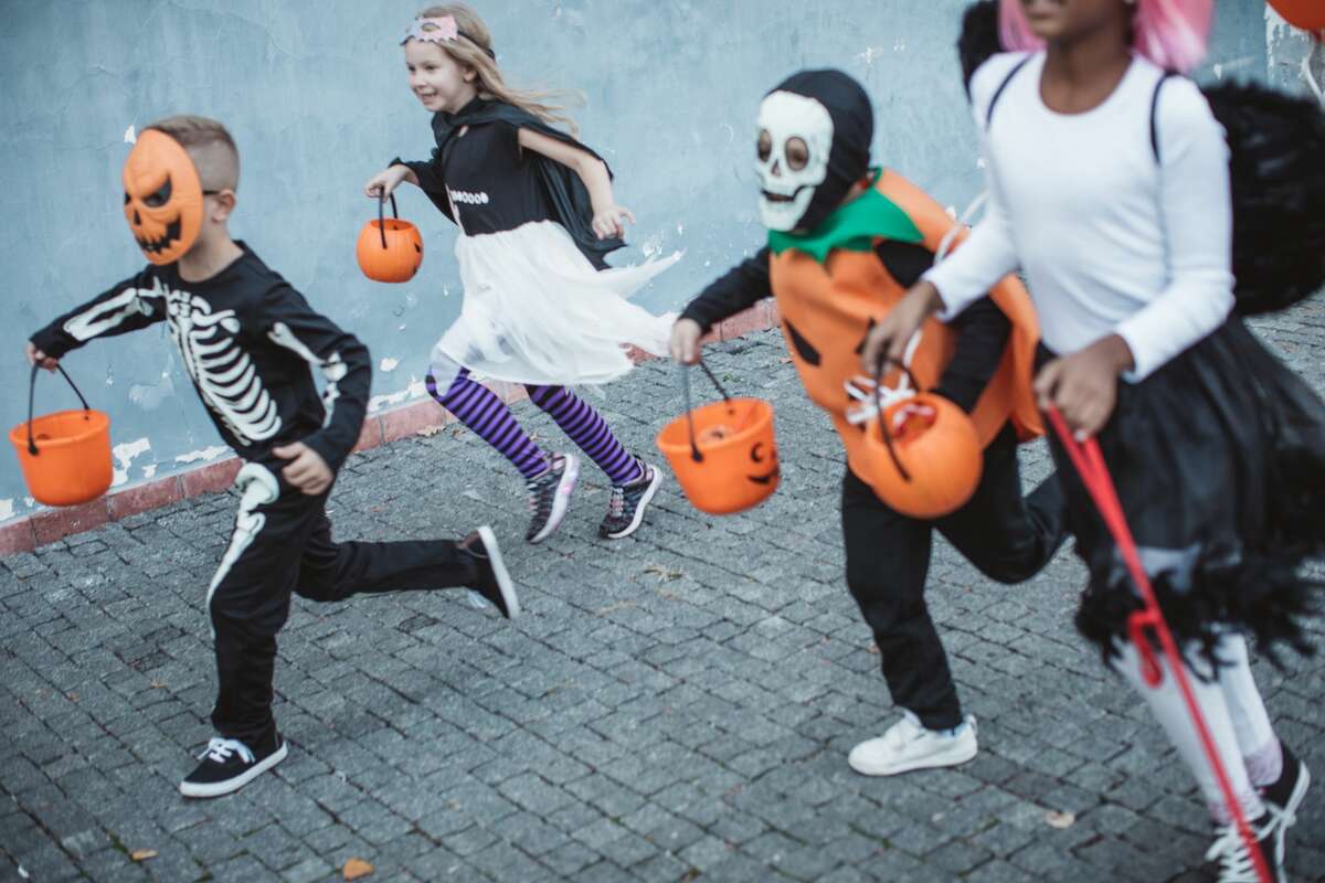 Group of children go trick or treating wearing costumes.