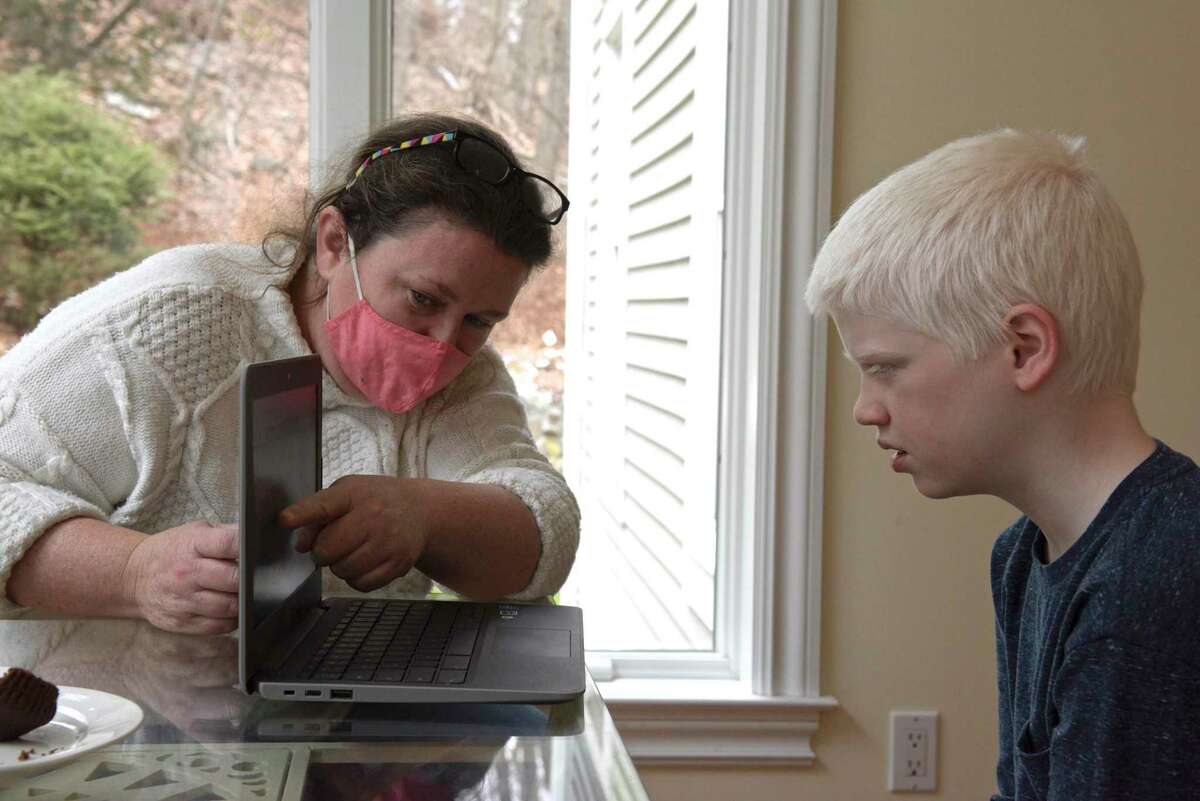 Helen Quinn works with her son James at their home on Wednesday, January 13, 2021, in Danbury, Conn. Danbury schools saved money last academic year on transportation, tutors and substitute teachers due to remote learning. Technology costs rose, however.